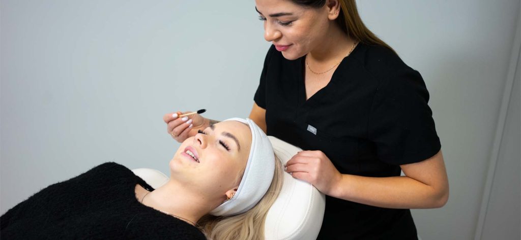 Kvinnen ligger komfortabelt på en av velbehags klinikker mens hun får et vippeløft av en hudpleier.