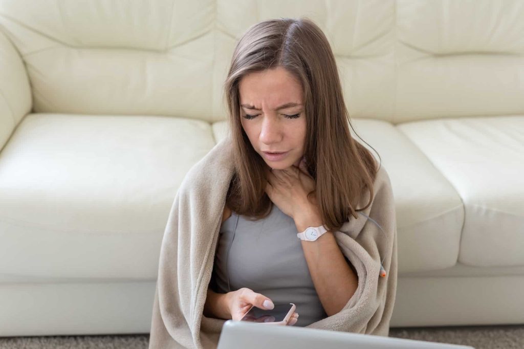 Woman having a sore throat sitting on the floor with laptop