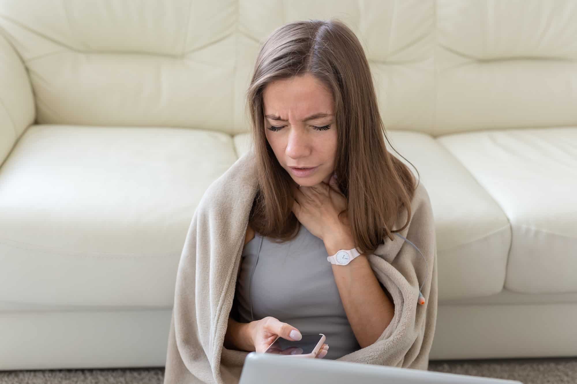 Woman having a sore throat sitting on the floor with laptop