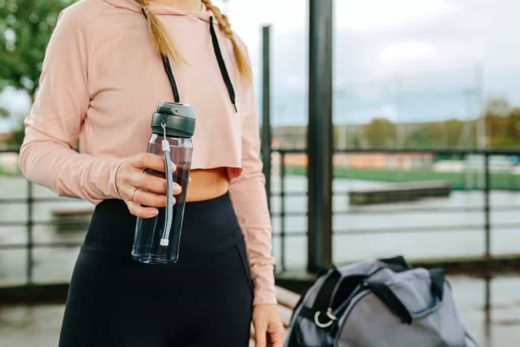 Young sportswoman with water bottle and gym bag
