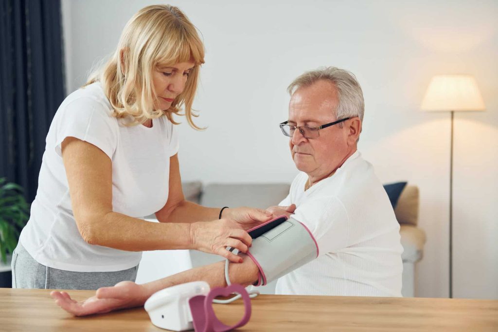 Wife measuring blood preasure of her husband. Senior man and woman is together at home
