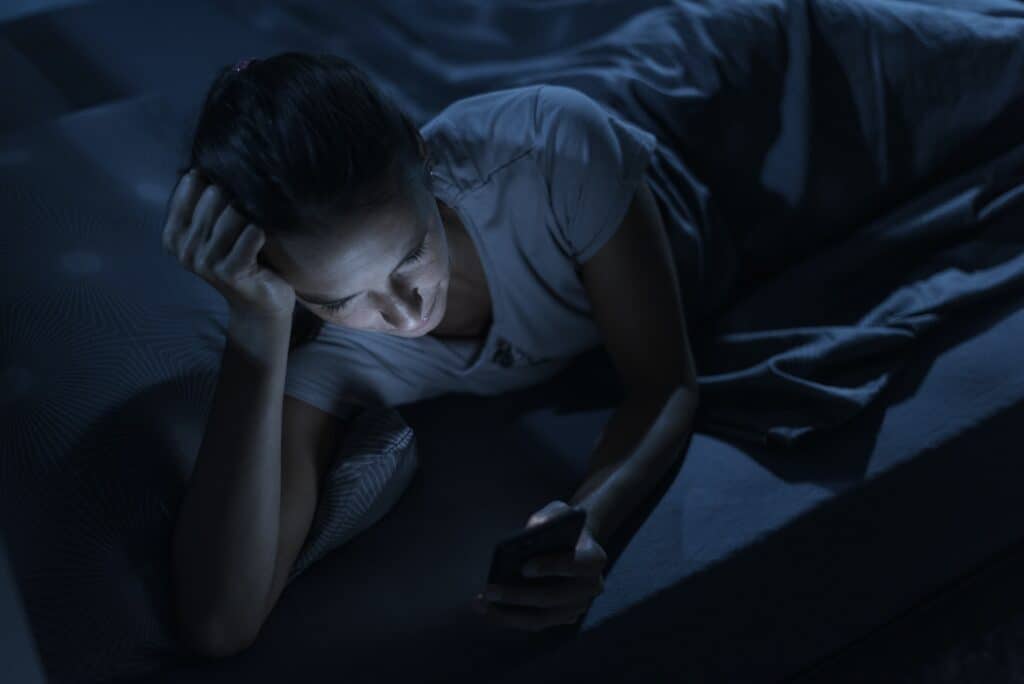 Woman lying in bed at night and connecting with her phone
