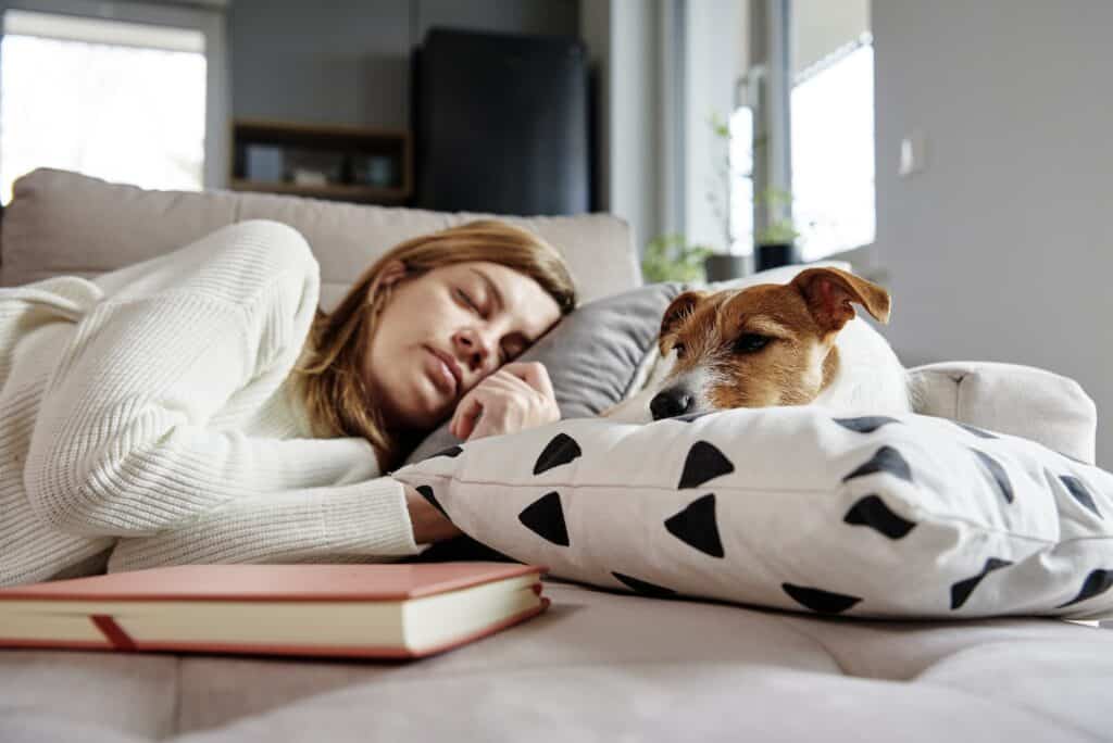Dame sover på sofaen med en hund. Hunden ser ut til å ha skabb.
