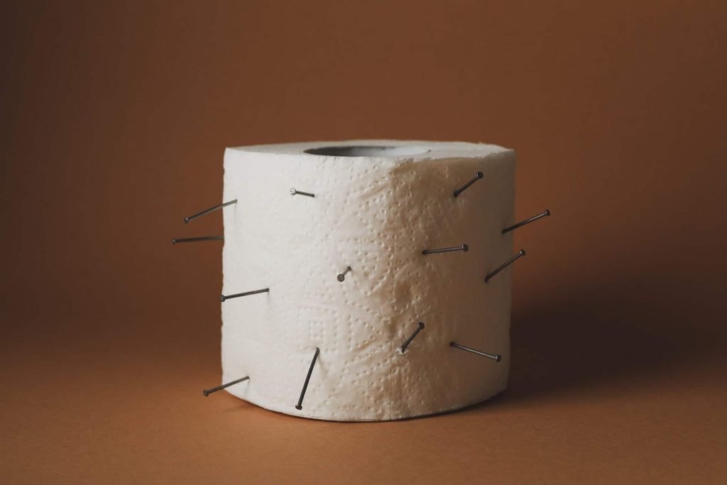 Toilet paper with nails on brown craft background. Hemorrhoids