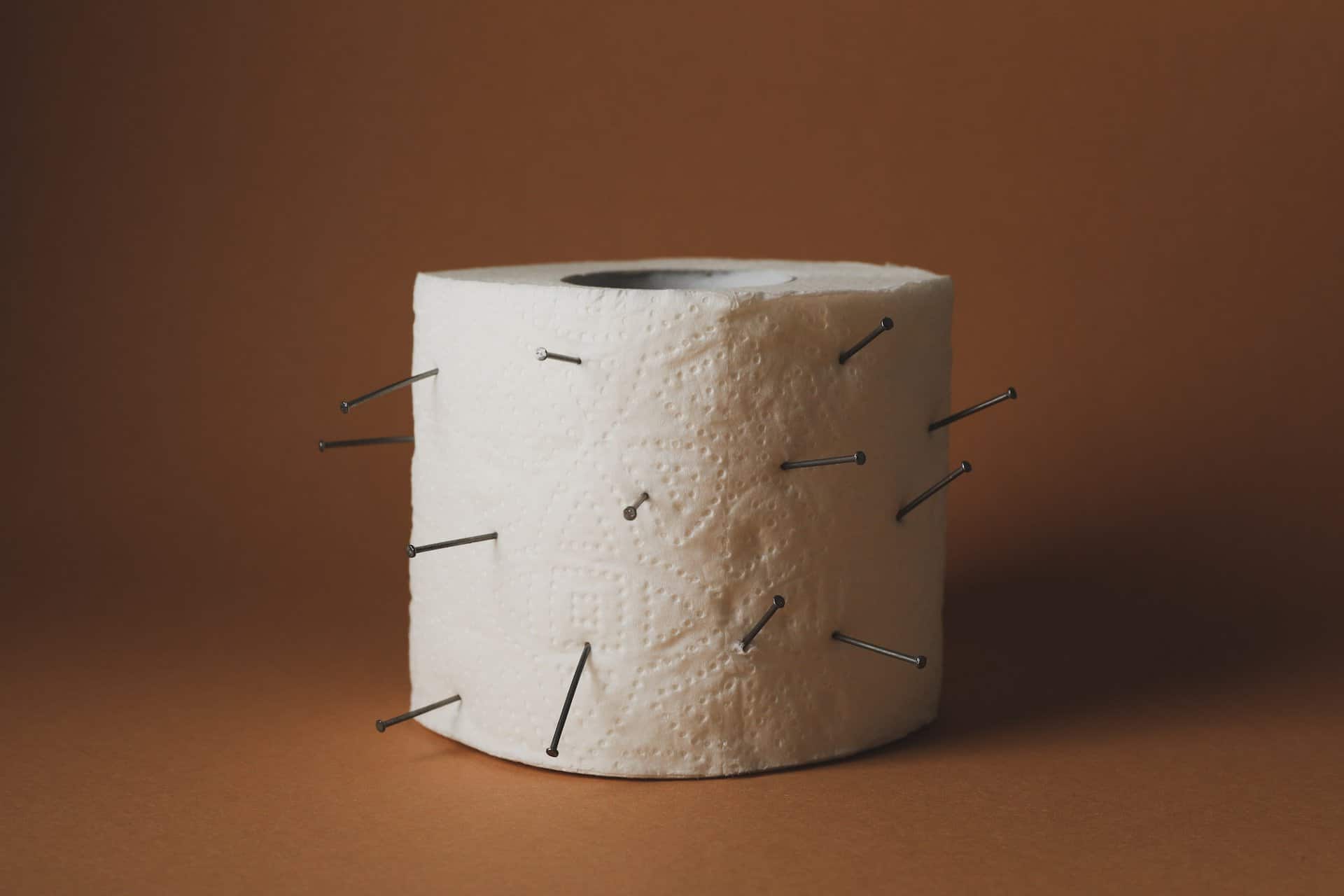 Toilet paper with nails on brown craft background. Hemorrhoids