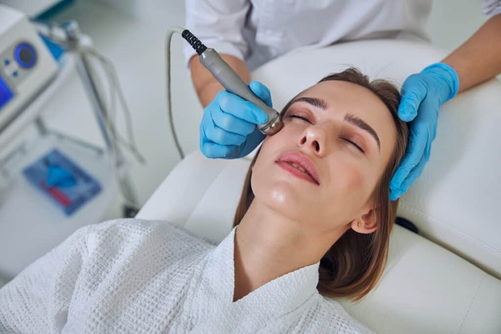 Adorable pretty lady receiving professional skin care with ultrasound device in beauty clinic