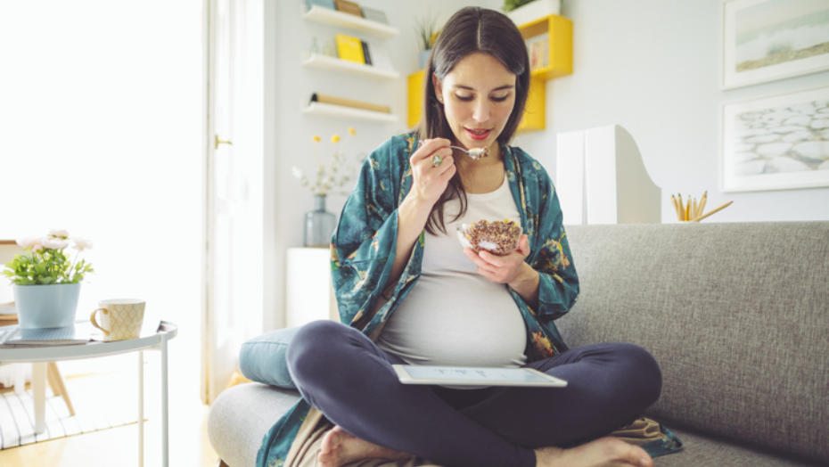 En ung gravid kvinne spiser yoghurt og musli en tidlig morgen.