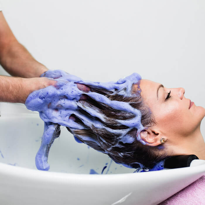 En dame er hos frisøren og får massert inn blå shampoo.