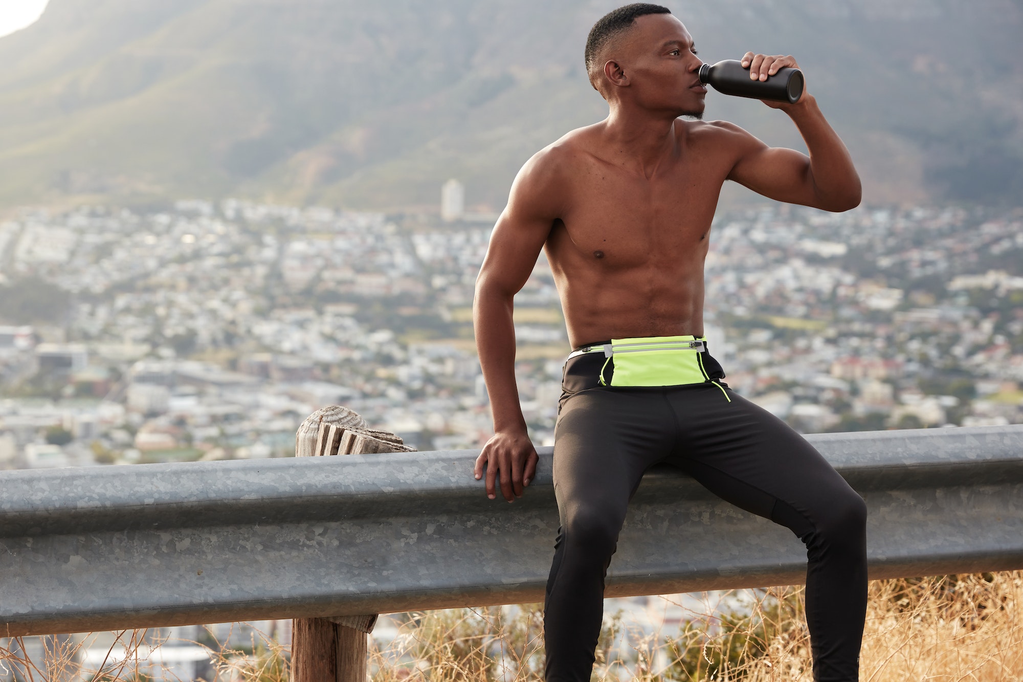 En mann drikker vann etter en lang joggetur, han har bare på seg skjorts fordi det er så varmt ute.