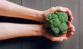 Brokkoli hjelper med b12 mangel. På dette bildet står en dame og viser en flott og grønn brokkoli.