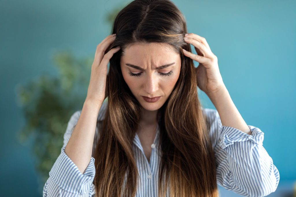 Frustrated young woman with headache and frowning while standing at home.