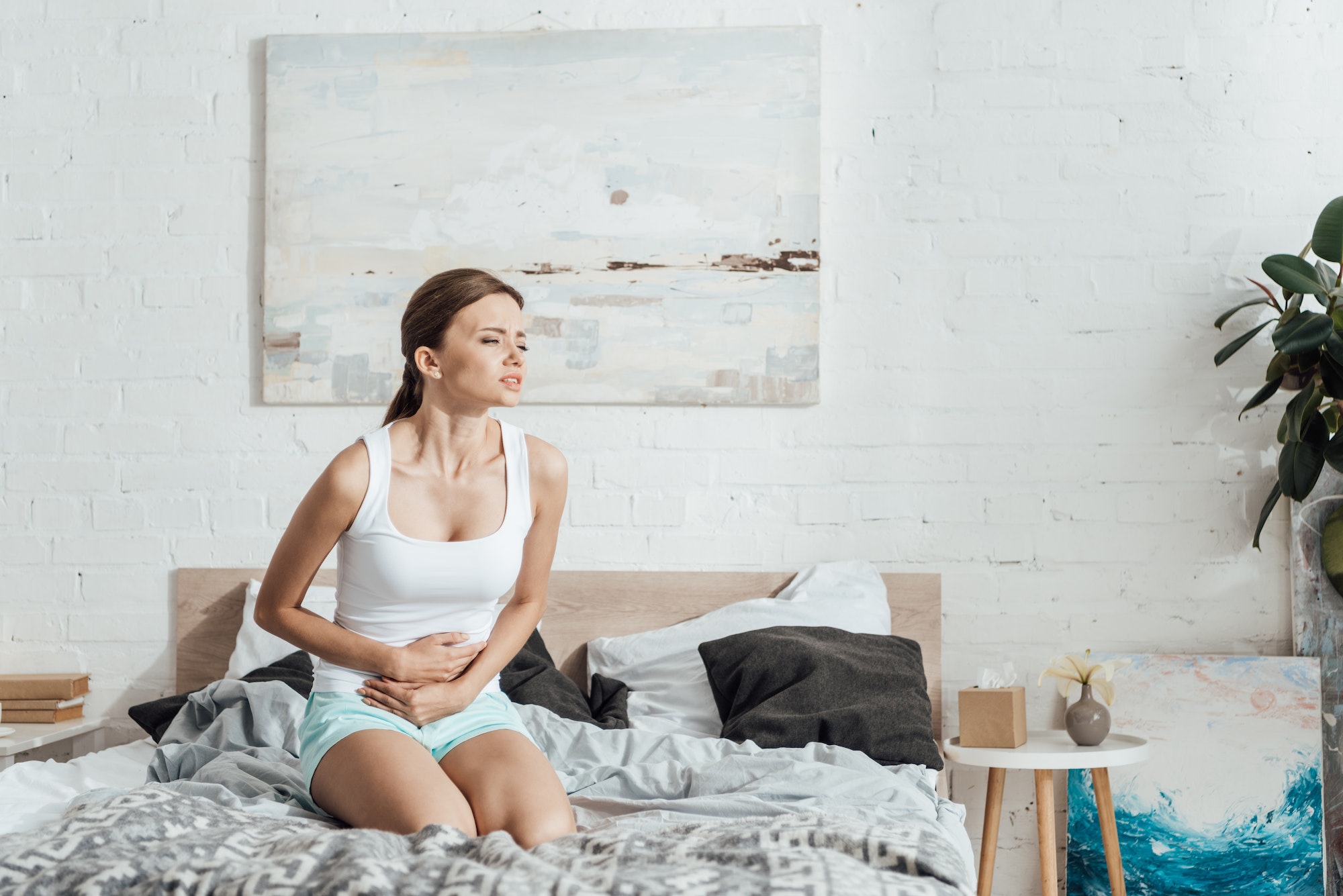 stressed young woman sitting on bed and touching belly