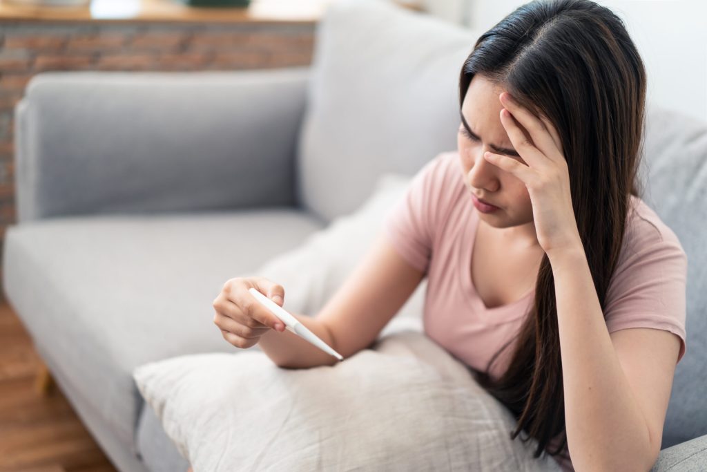 Unhealthy Asian young girl has a fever sittng on sofa at home.