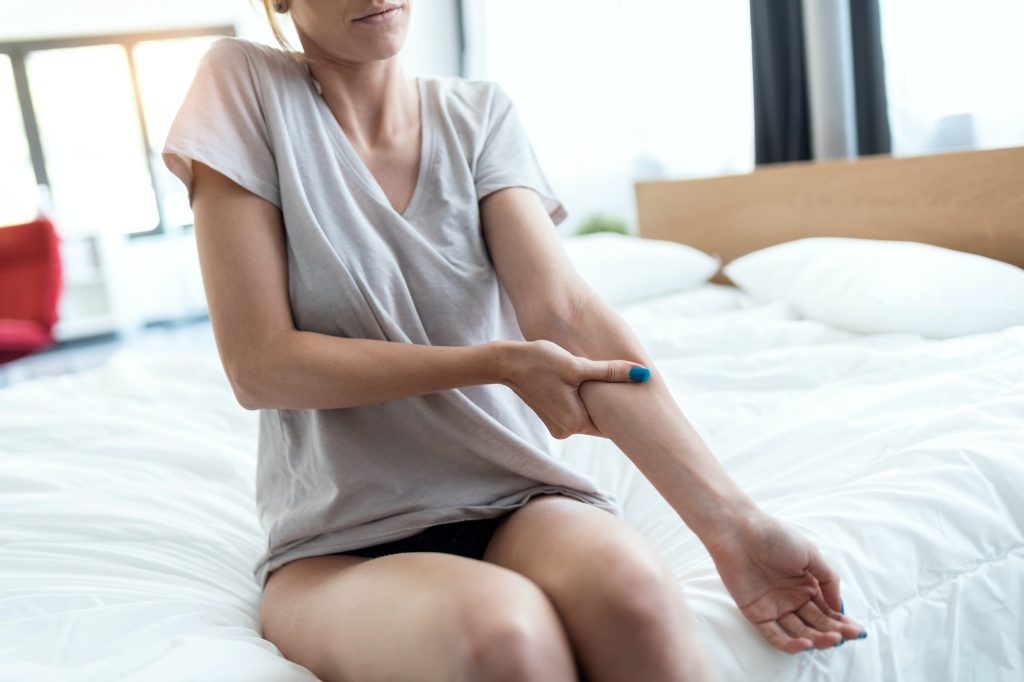 Young woman sitting on the bed with muscle pain. Fibromyalgia concepts.