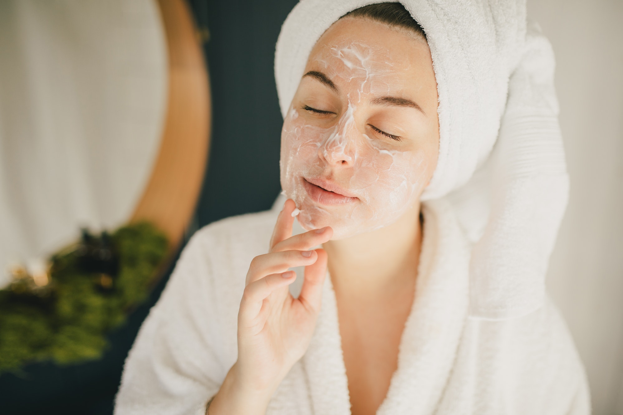 Young woman wearing bathrobe applying moisture on face. Treat yourself. Beauty rituals.
