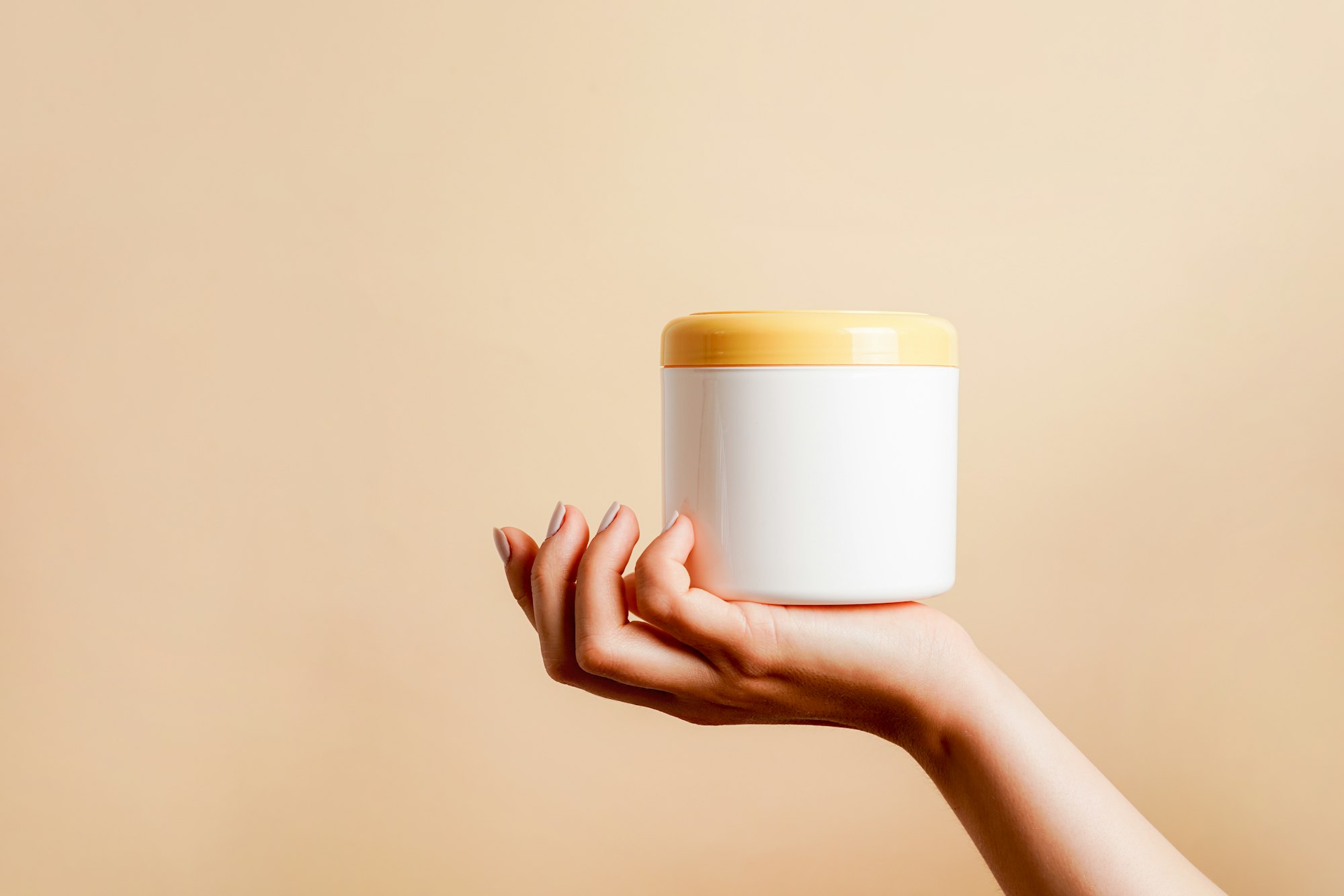 Closeup of woman hand holding a white bottle with nourishing mask for applying to hair or skin