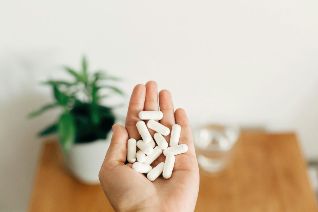 Hand holding magnesium capsule above glass of water on wooden table